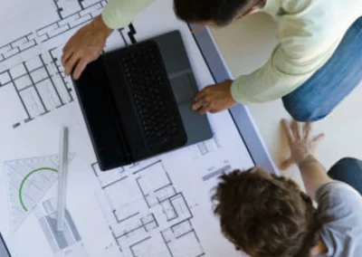 People sitting on floor looking at building blueprints, and a laptop