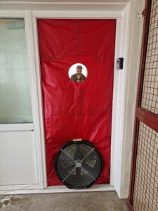 A red cloth with a fan attached to the bottom covers a doorway, with a person visible through a round window near the top.
