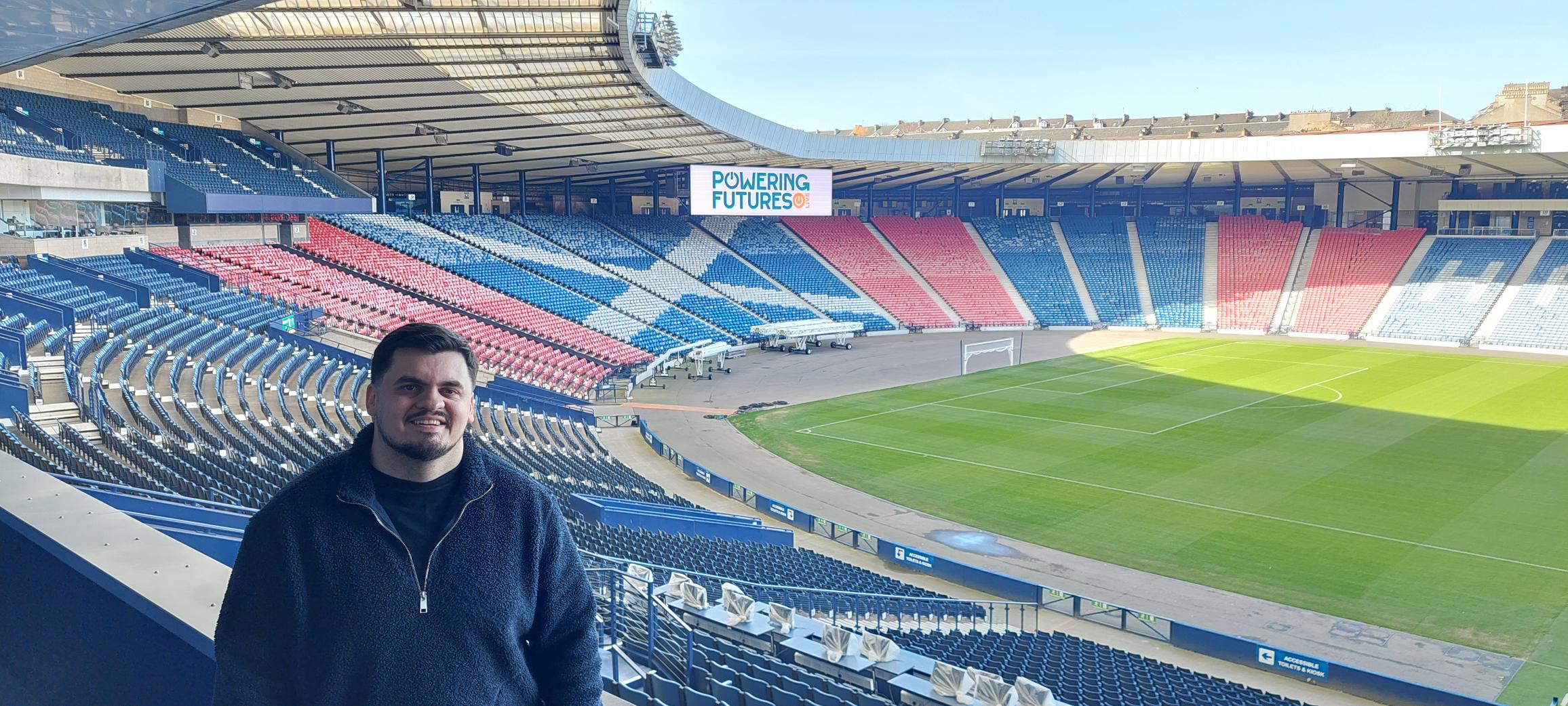 A man in the stands at Hampden Park, with the stadium behind him