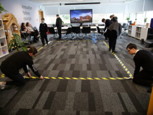 Young people measure out a rectangle on the floor using yellow and black striped tape