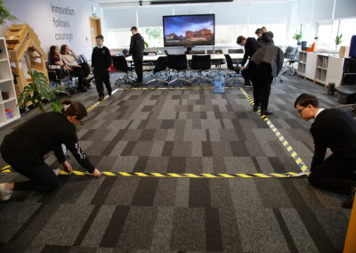 Young people measure out a rectangle on the floor using yellow and black striped tape