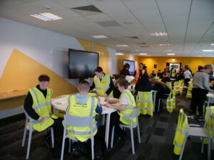 Young people in high-vis vests participate in an activity around a table