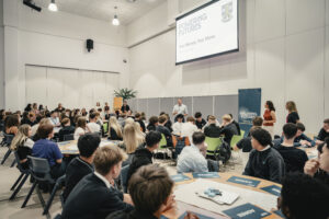 Groups of pupils sit at tables, in a large conference room-type setting, taking part in a Powering Futures activity